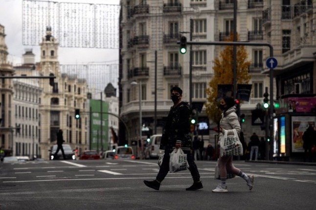 Des personnes marchent avec des sacs d'épicerie sous les lumières de Noël dans le centre de Madrid.