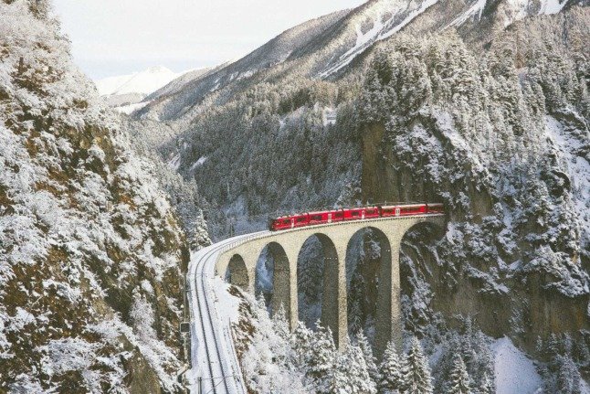 Un train rouge se fraie un chemin à travers les montagnes suisses par un jour de neige. 