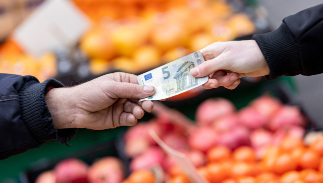 Dans un supermarché, un client tend un billet de 5 €.
