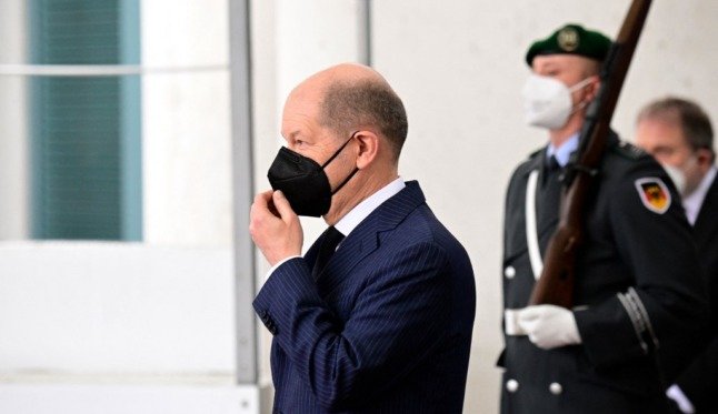 Olaf Scholz masqué devant des gardes armés.