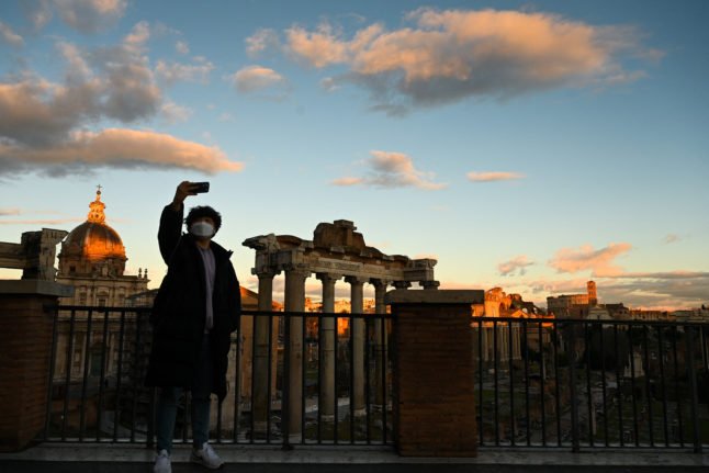 Un touriste masqué prend un selfie au coucher du soleil devant l'ancien forum de Rome.