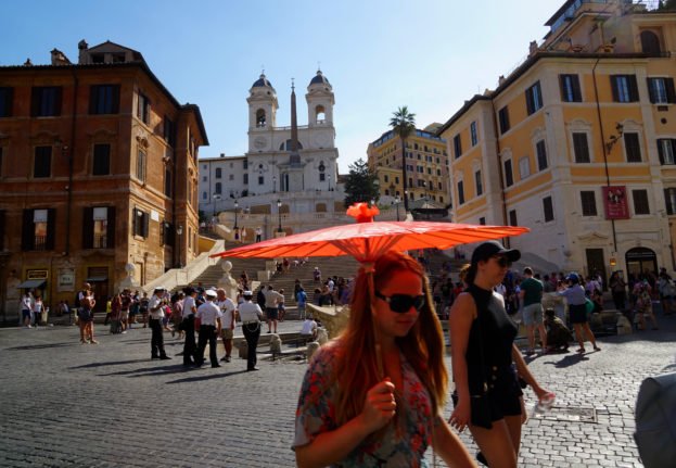 Une touriste se protège du soleil avec un parapluie en papier alors qu'elle marche sur la Piazza di Spagna près de la Place d'Espagne à Rome. 