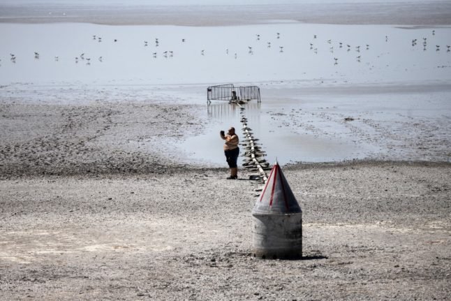Un homme prend une photo debout sur le fond du lac asséché du Zicksee à St. Andrae am Zicksee dans le Burgenland, en Autriche, le 20 juillet 2022. - La chaleur continue a entraîné l'assèchement du lac. Des centaines de poissons sont morts dans le lac asséché. (Photo par Alex HALADA / AFP)