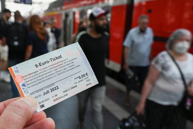 Une personne tient le billet à 9 € devant un train régional à Francfort.