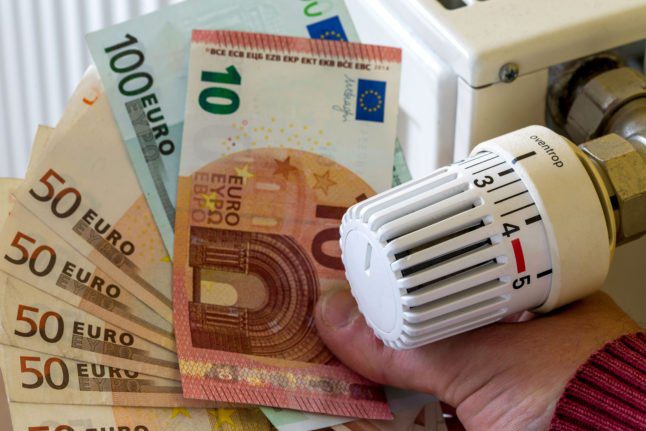 Un homme tient une liasse de billets en euros à côté d'un radiateur.