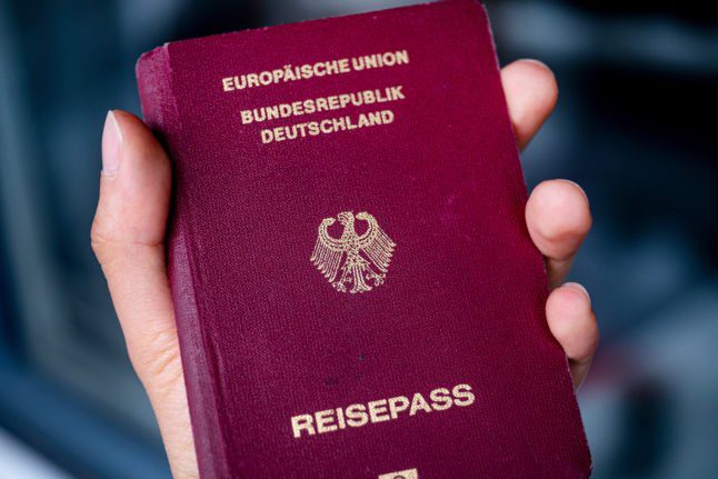 Un homme tient un passeport allemand dans sa main.