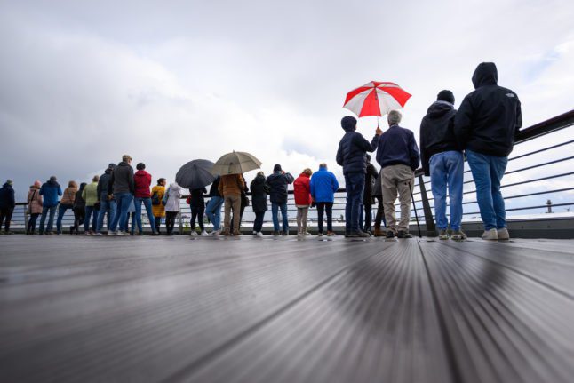 Des personnes se tiennent avec des parapluies sous des nuages gris au centre de croisière de Hambourg Altona.
