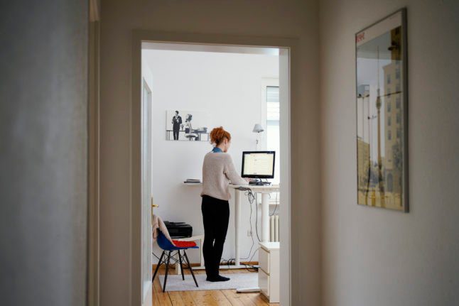 Une femme utilise le plan de travail de sa cuisine comme bureau debout pour travailler à domicile.