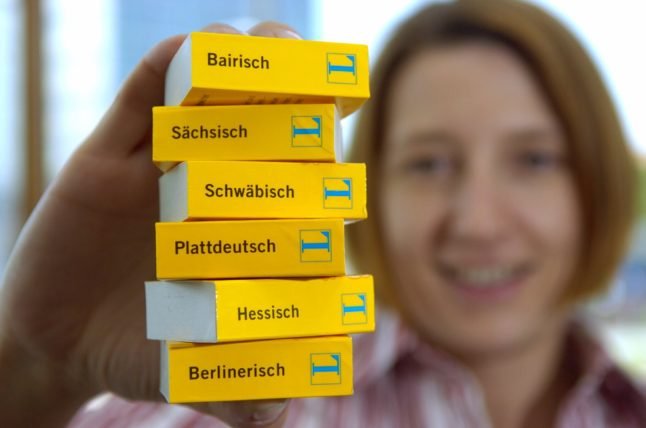 Une femme tient des éditions de dictionnaires avec différents dialectes allemands.
