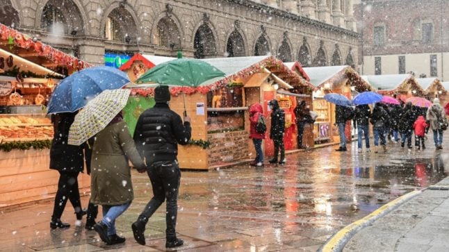 Les gens traversent un marché de Noël au centre-ville de Milan alors que la neige tombe le 8 décembre 2021. 